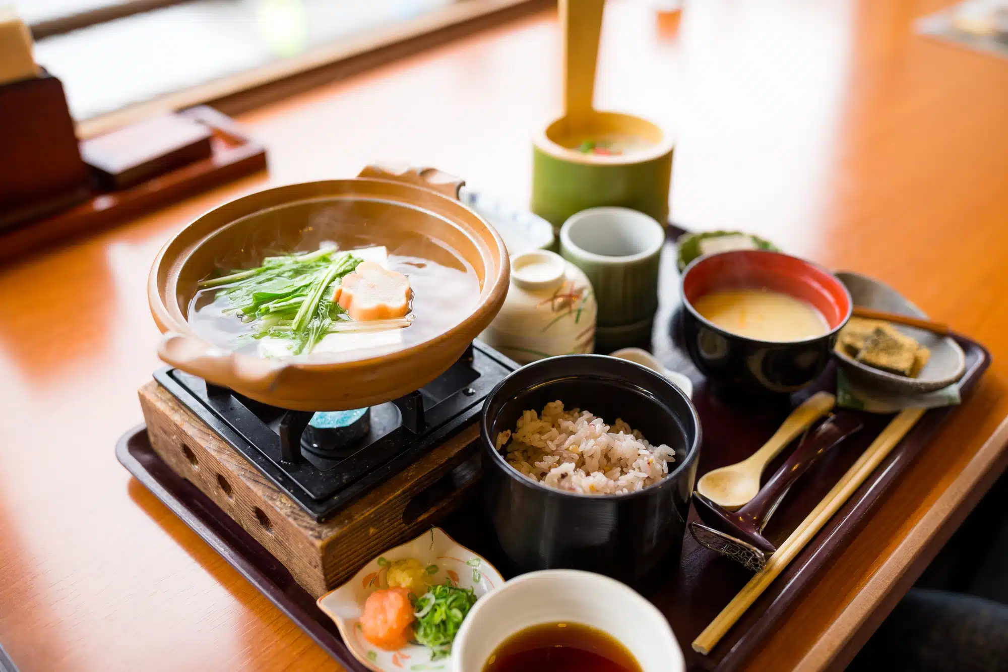 Hand-thrown bowls of grains, greens, and broth set on a wooden table, suggesting the slow, ritualized Okinawan practice of eating until 80% full.