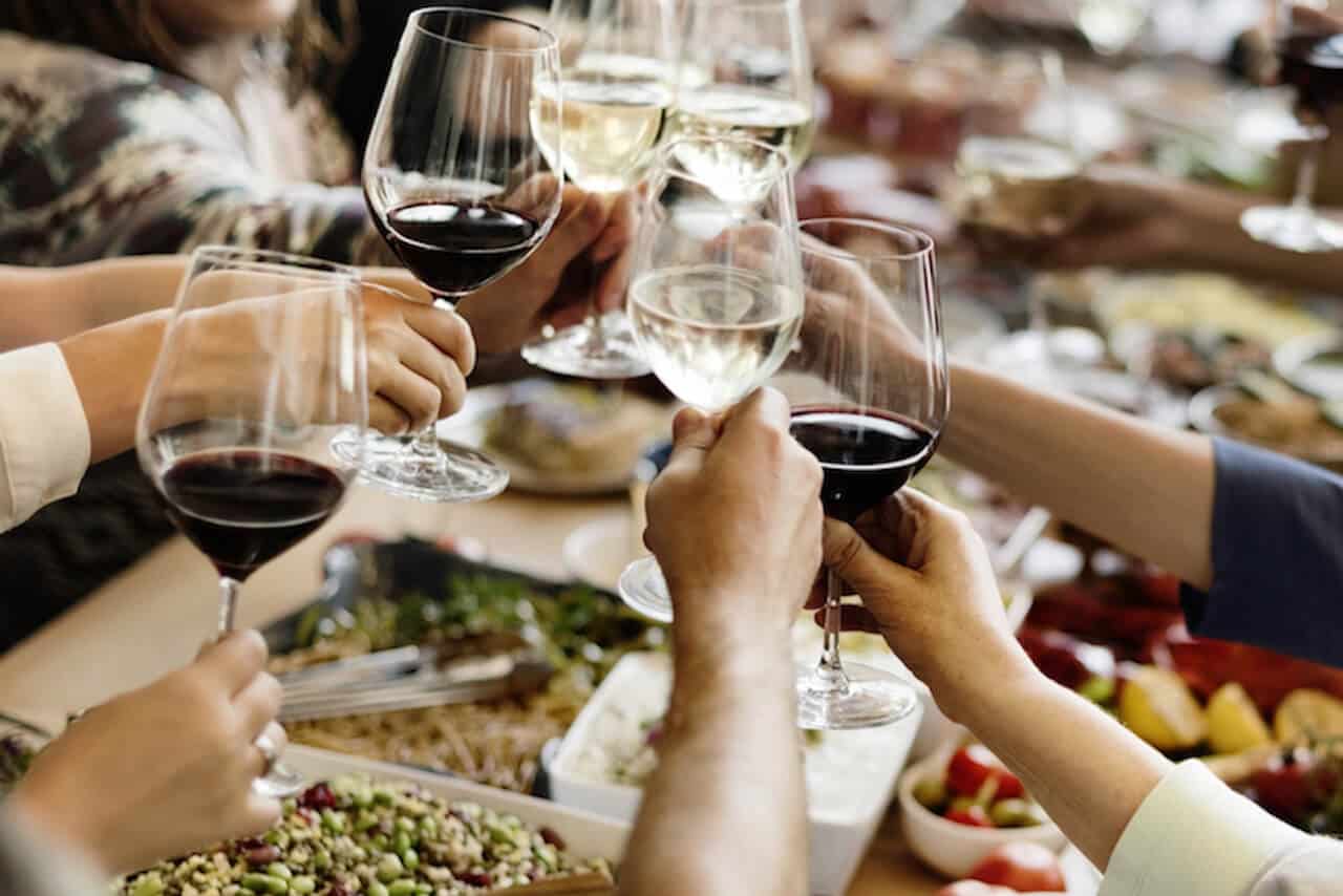Friends gathered around a long candlelit table sharing food and drink, capturing the five-o'clock social ritual at the heart of Sardinian and Ikarian longevity.